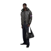 Man wearing stylish gray leather bomber jacket with hood, holding black shoulder bag, modern urban fashion