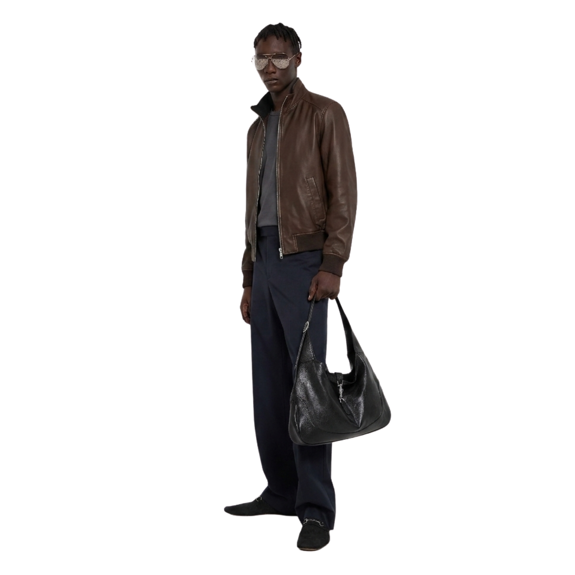Man wearing brown leather bomber jacket, dark trousers, holding black shoulder bag, stylish casual outfit