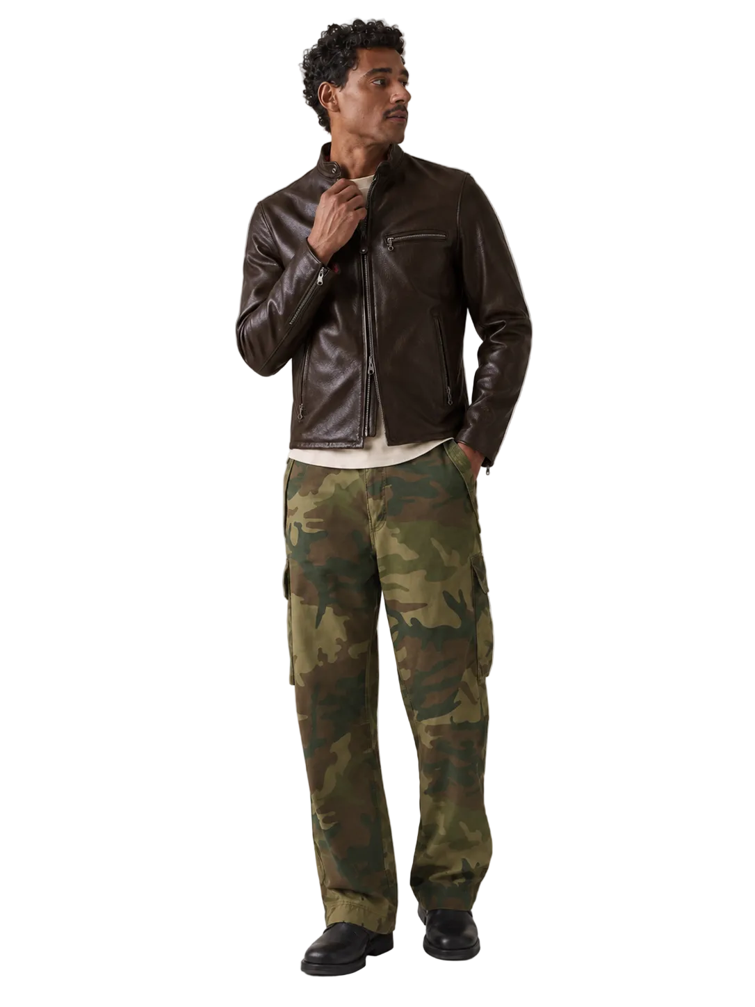 A man modeling a dark brown leather jacket and green camouflage cargo pants against a neutral gray studio background.