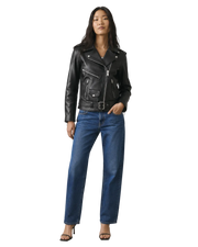 Woman wearing black leather moto jacket with belt, blue jeans, and heels