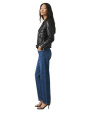 Woman in black leather moto jacket and wide-leg blue jeans, side view