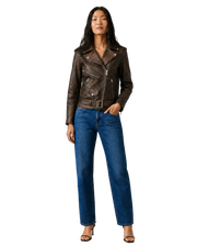 Woman in brown leather moto jacket with belt, paired with blue wide-leg jeans and heels