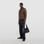 Man in brown leather jacket holding black shoulder bag, stylish casual outfit