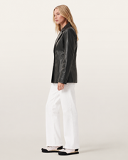 Woman in black leather jacket, white wide-leg jeans, and sneakers, side view