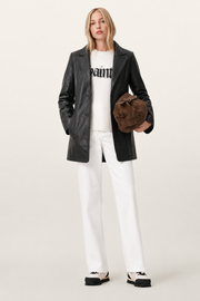 Woman in black leather jacket, white graphic sweater, white pants, and brown suede bag