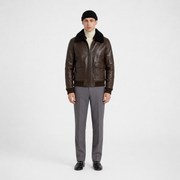 Men's brown leather bomber jacket with shearling collar, styled with turtleneck and gray trousers