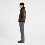 Man wearing brown leather bomber jacket with shearling collar, gray trousers, black beanie, and loafers