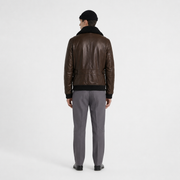 Men's brown leather bomber jacket with shearling collar, back view, paired with gray trousers and black beanie