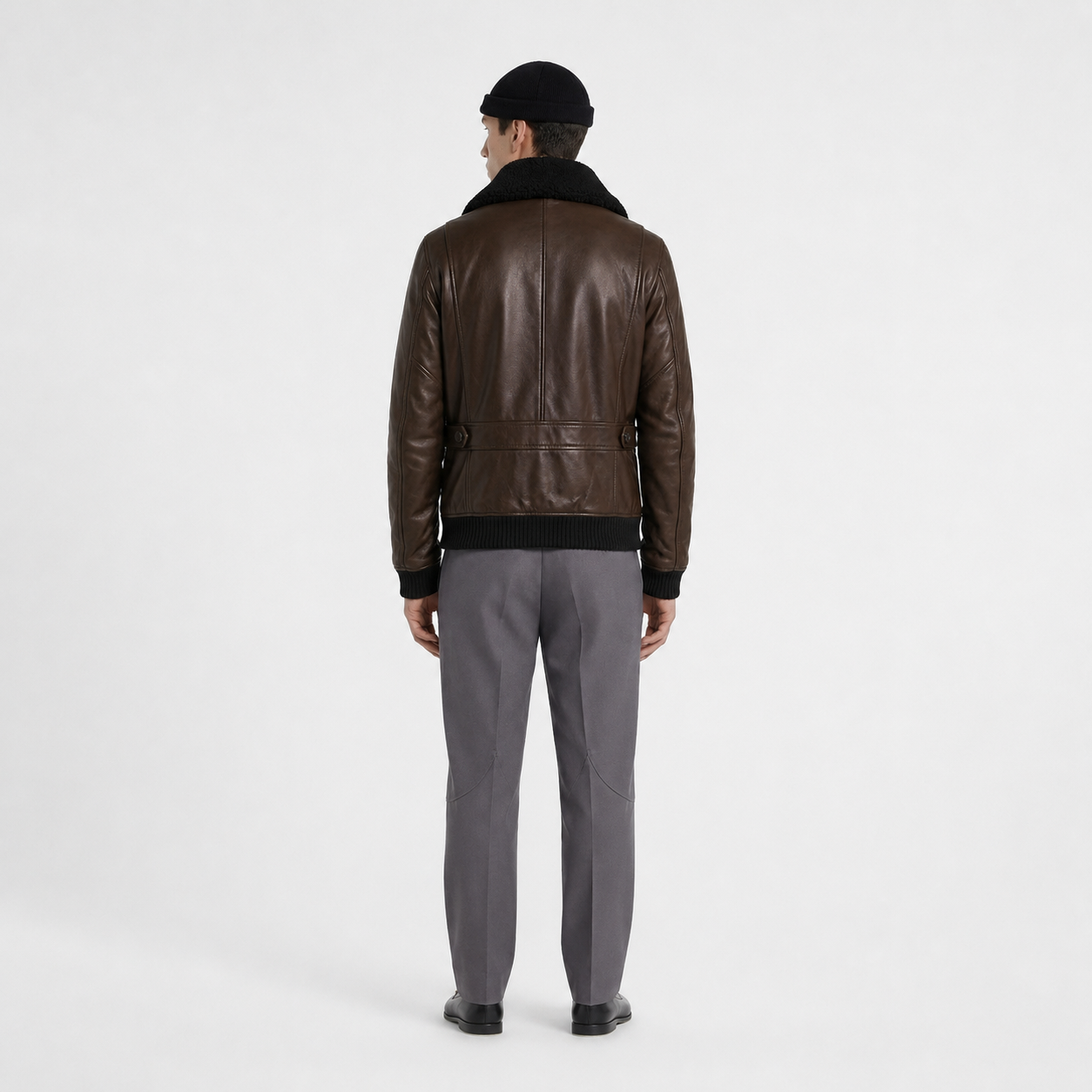 Men's brown leather bomber jacket with shearling collar, back view, paired with gray trousers and black beanie