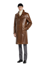 Men's brown leather trench coat with classic collar, front buttons, and pockets, styled with beanie and loafers