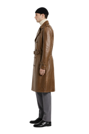 Men's brown leather trench coat with belt, styled with beanie and gray trousers