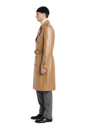 Men's tan leather trench coat with belt, worn with beanie and gray trousers