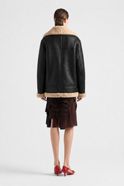 Black shearling coat with cream fur trim, worn with ruffled skirt and red heels, back view