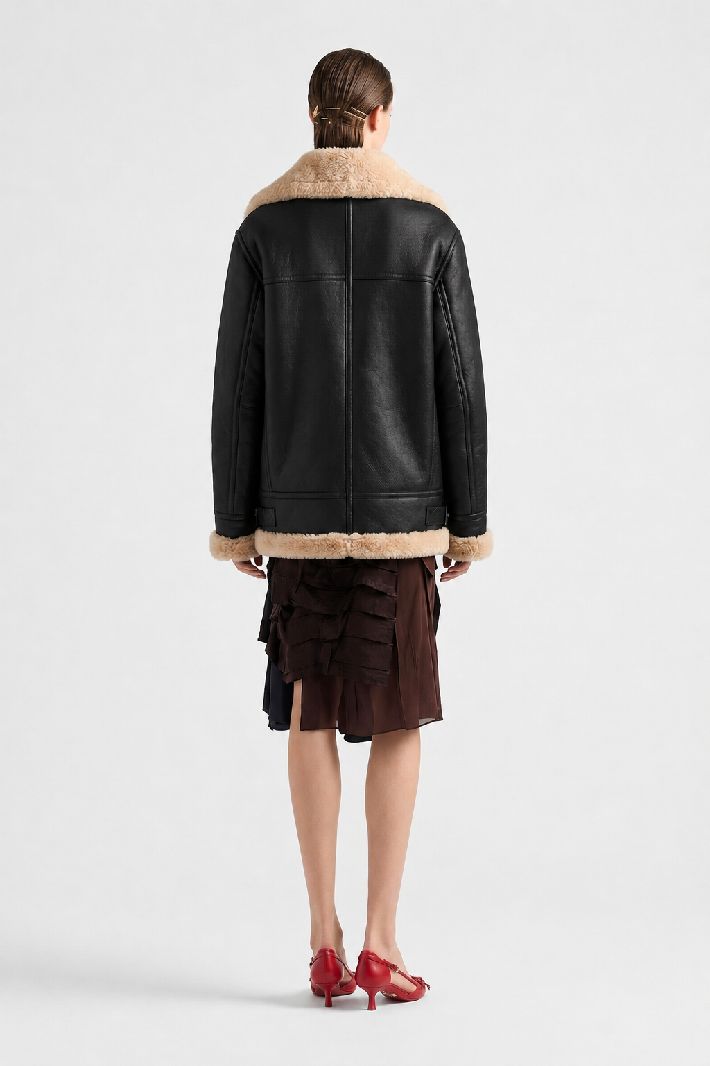 Black shearling coat with cream fur trim, worn with ruffled skirt and red heels, back view