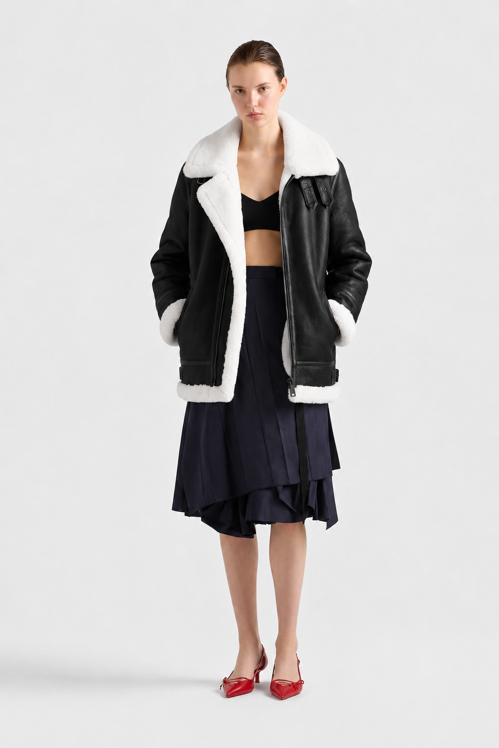 Black shearling aviator jacket with white fur trim, styled with navy pleated skirt and red heels