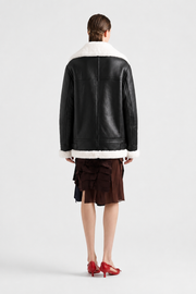 Black shearling coat with white fur trim, back view, paired with ruffled skirt and red heels