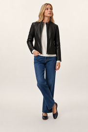 Woman in black leather jacket, white sweater, and blue wide-leg jeans, standing against neutral background