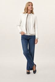 Woman wearing white leather jacket, blue jeans, and flats, styled for casual fashion