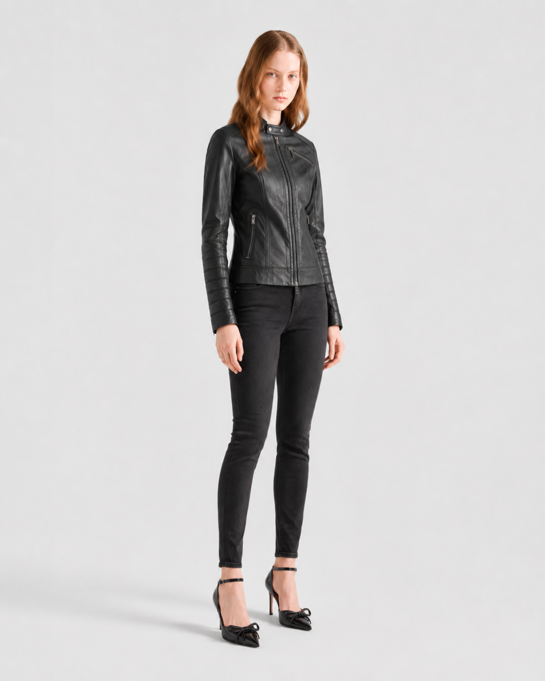 Woman in black leather moto jacket, skinny jeans, and bow heels on white background