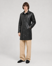 Man wearing black leather trench coat with button front, paired with beige pants and loafers