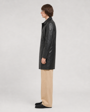 Man in black leather trench coat with beige pants and loafers, side profile