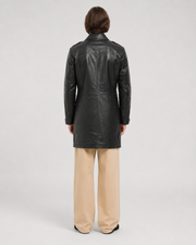 Black leather trench coat back view, styled with beige wide-leg pants for modern outerwear look