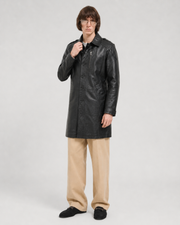 Man wearing black leather trench coat with button front, paired with beige pants and loafers