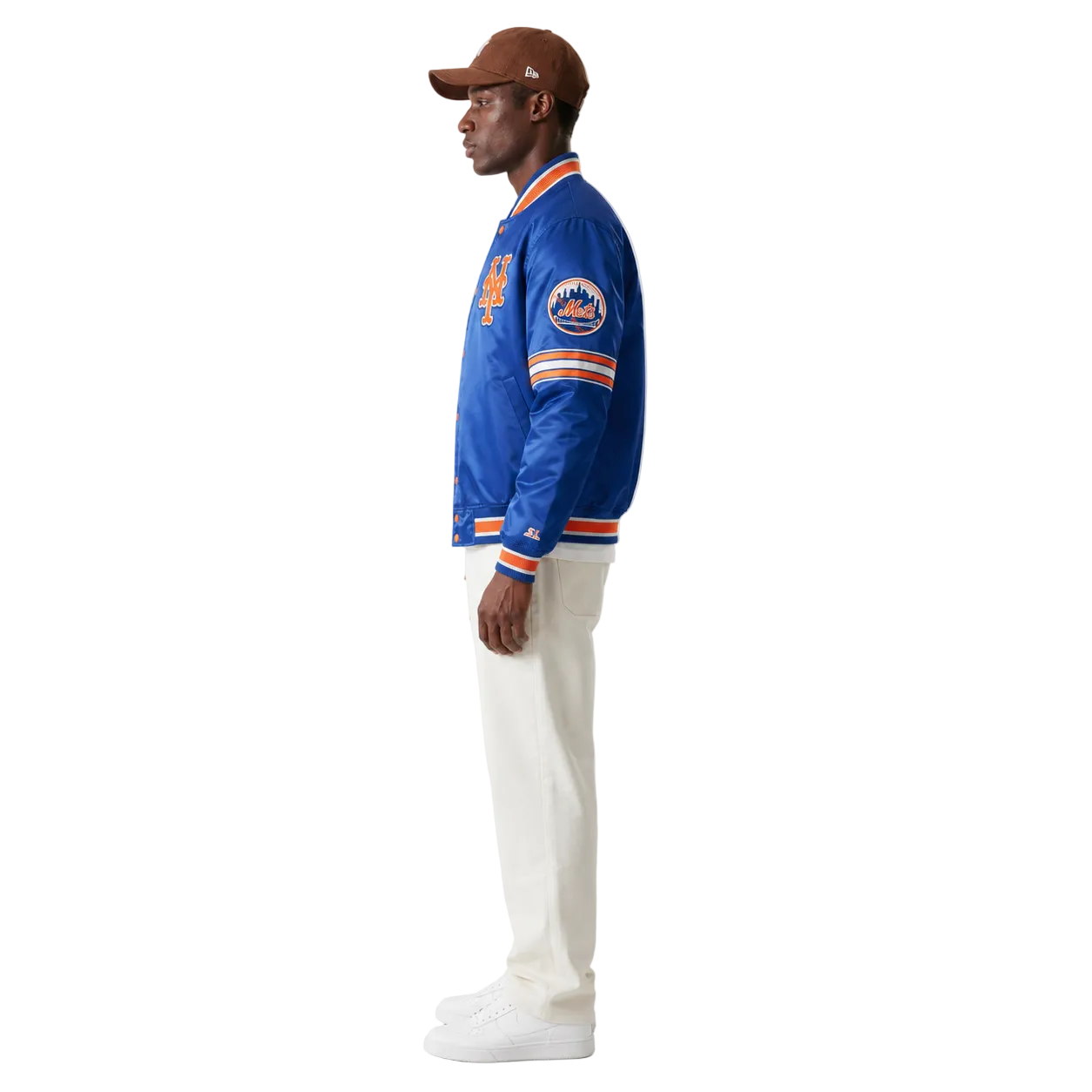 Man wearing blue New York Mets varsity jacket with orange trim, white pants, and brown cap