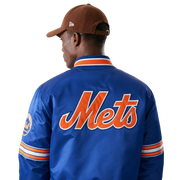 Blue Mets varsity jacket with orange script logo, striped sleeves, and team patch, worn with brown cap