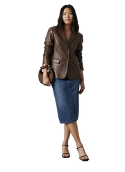 Woman in brown leather blazer, denim midi skirt, black heels, and matching handbag, studio fashion look