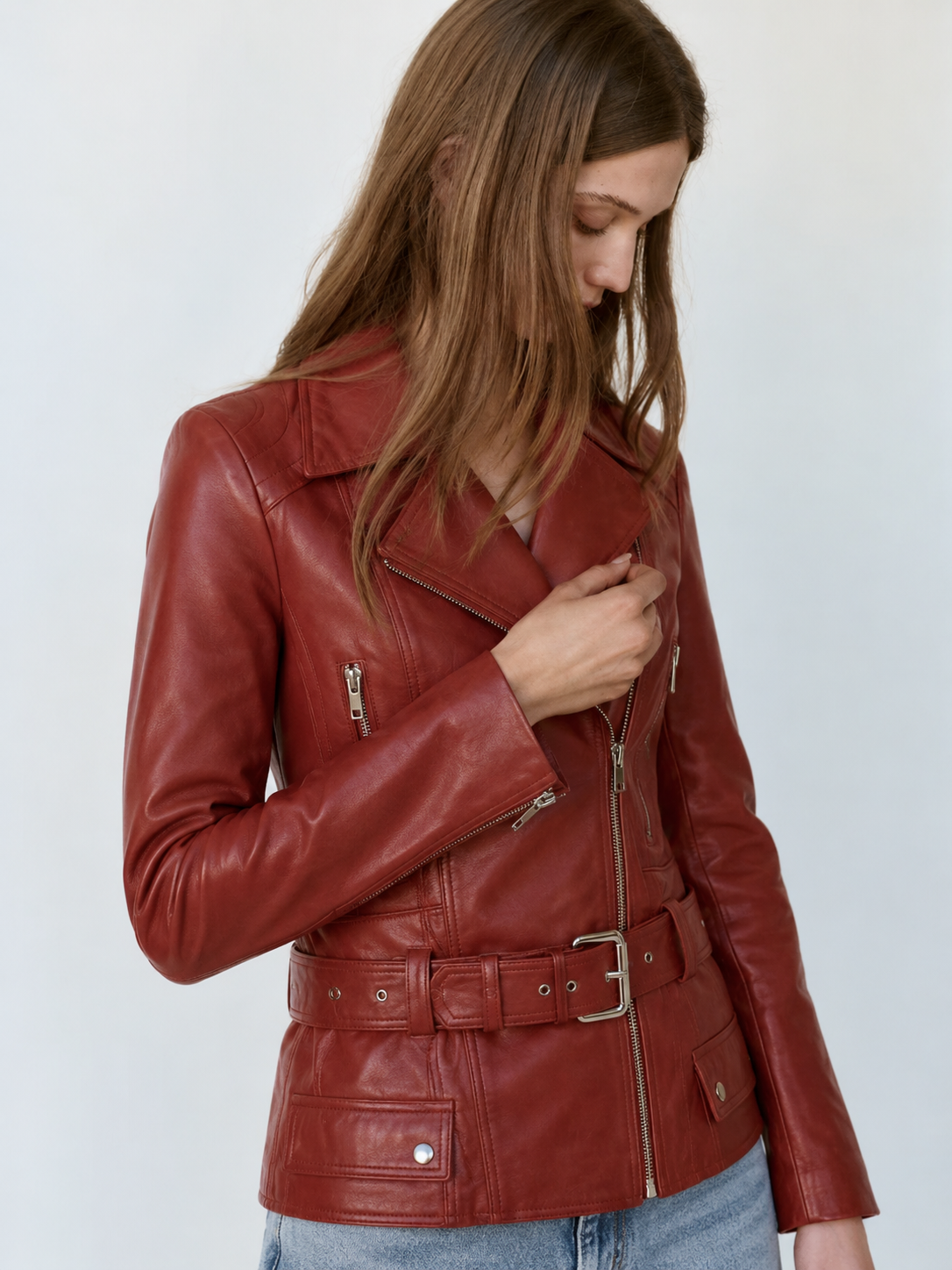 Woman wearing red leather biker jacket with belt and zippers, styled with jeans