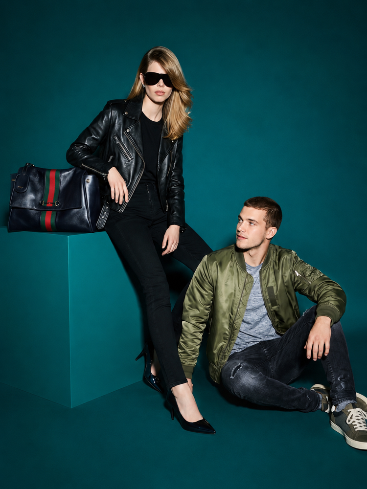 Stylish couple in leather jackets with designer handbag on teal background
