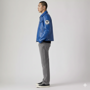 Man wearing blue leather jacket with patch, gray jeans, and black sneakers