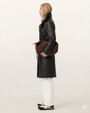 Woman in black leather coat with brown suede bag, white pants, and sneakers