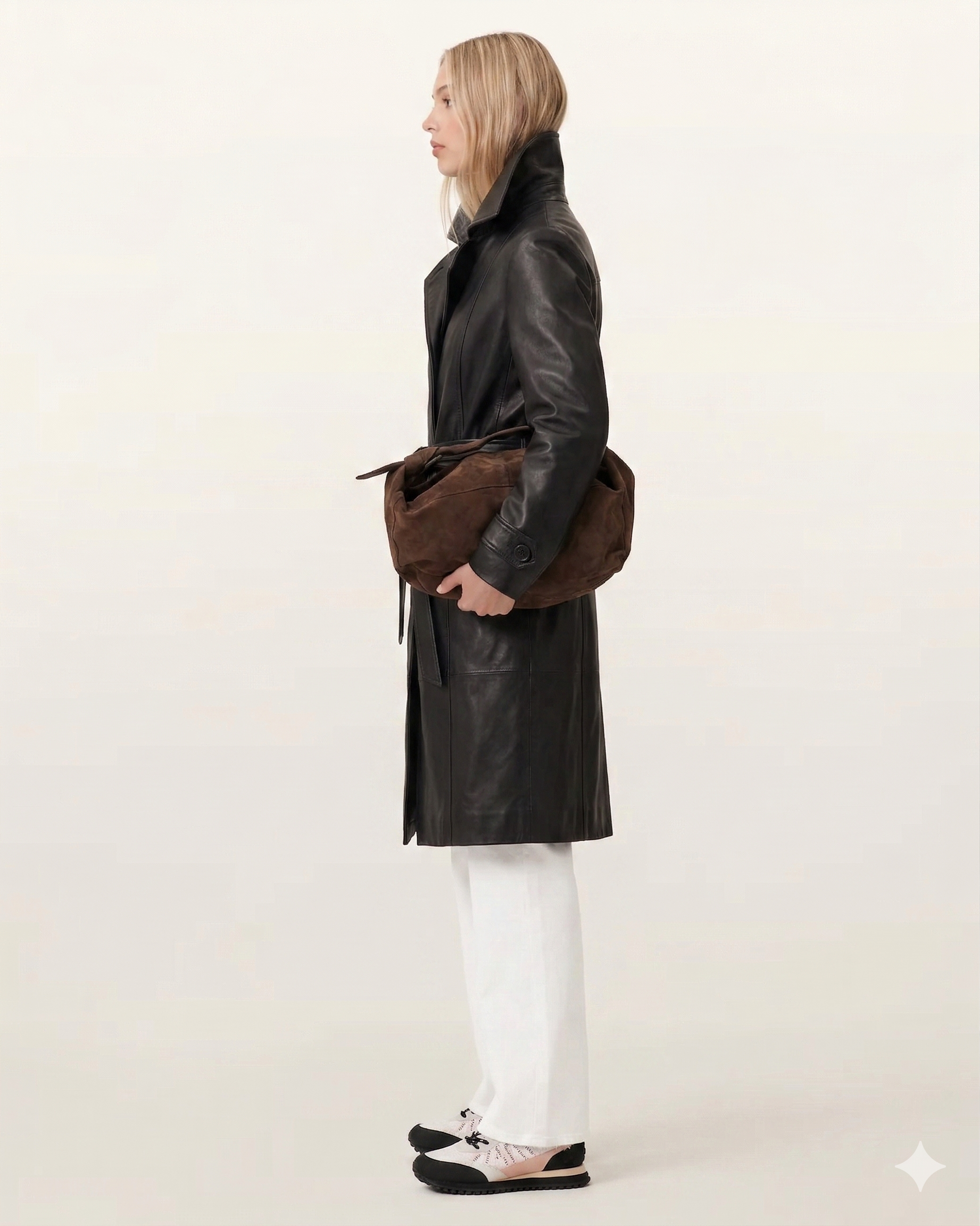 Woman in black leather coat with brown suede bag, white pants, and sneakers