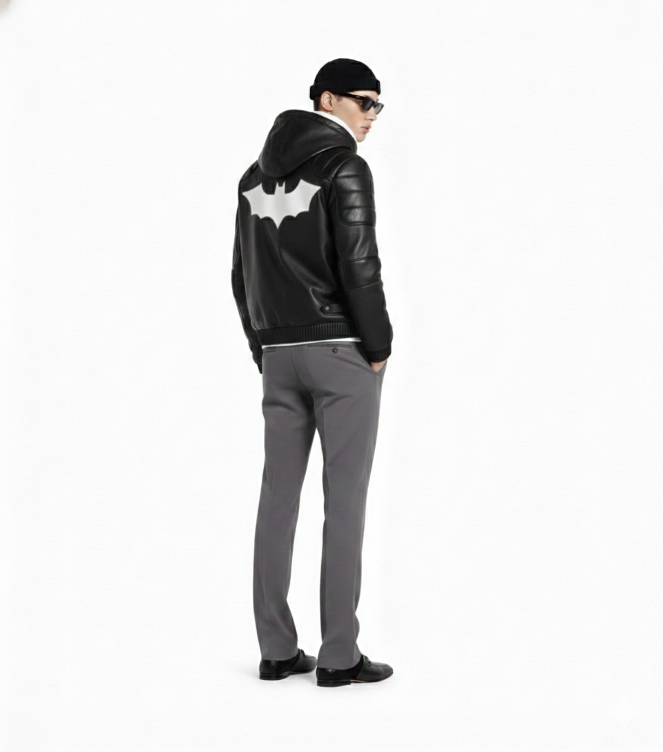 Man wearing black leather hoodie jacket with white bat emblem, gray pants, sunglasses, and beanie