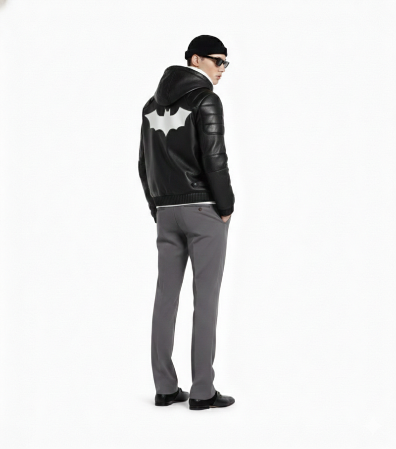 Man wearing black leather hoodie jacket with white bat emblem, gray pants, sunglasses, and beanie