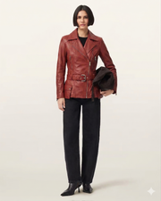 Woman in red leather moto jacket with belt, black jeans, and heels, holding hat