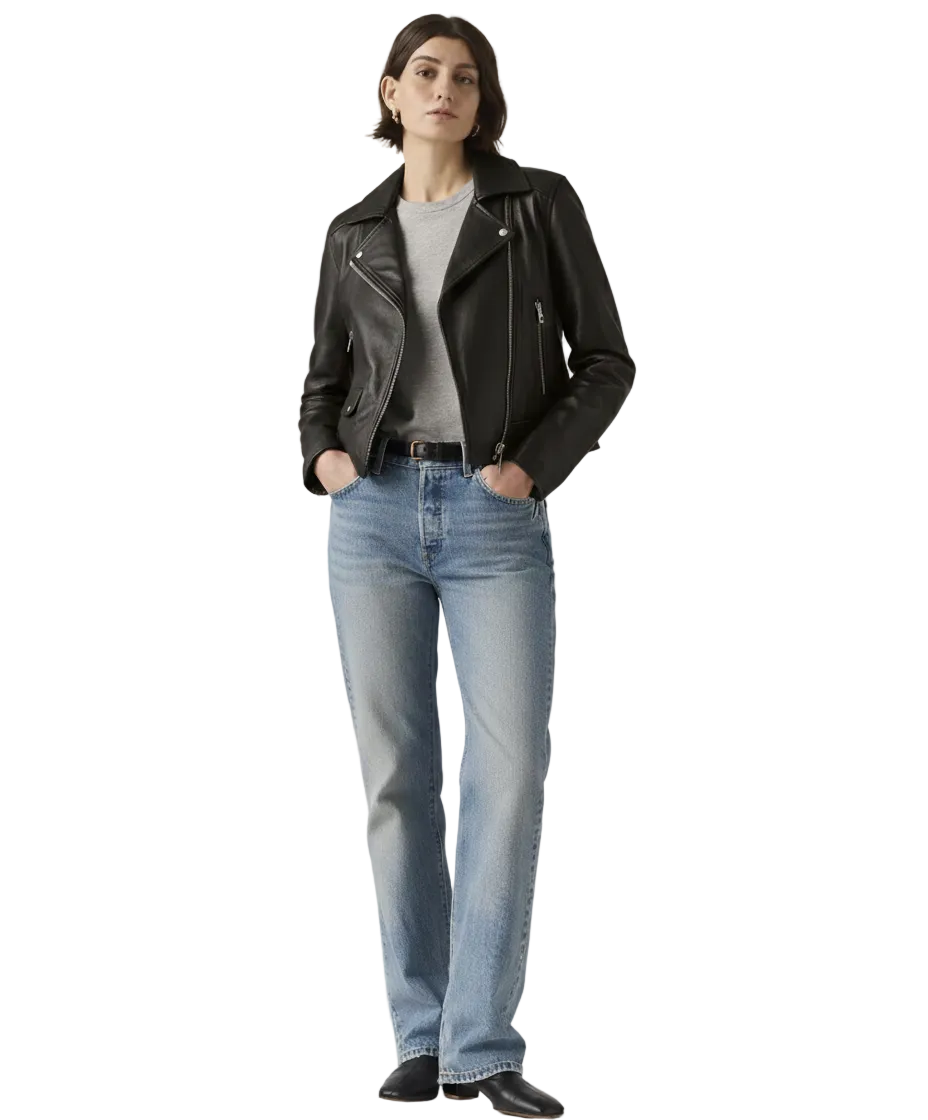 Woman wearing black leather jacket, gray tee, and blue jeans with hands in pockets