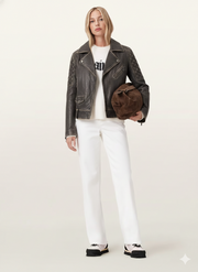 Woman in distressed leather moto jacket, white jeans, and chunky sneakers holding brown suede bag