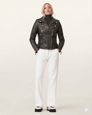 Woman in black quilted leather biker jacket with gold zippers, white pants, and chunky sneakers