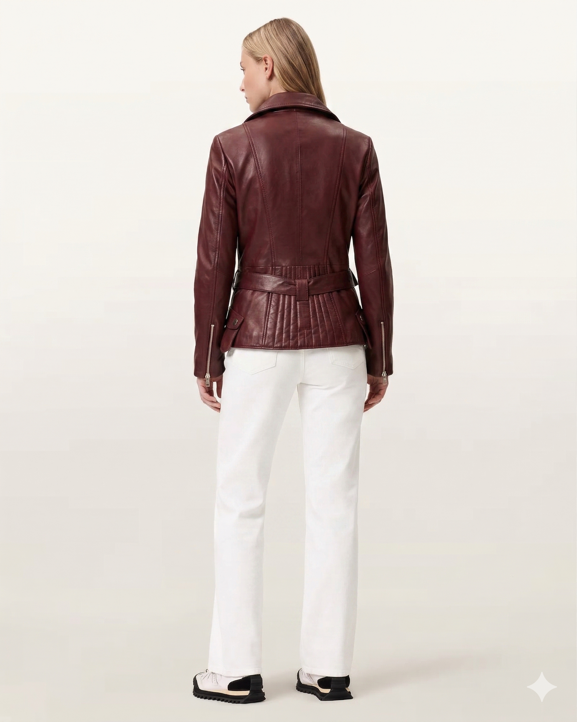 Woman wearing burgundy leather moto jacket with belt back view, paired with white pants