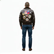 Men's brown leather bomber jacket with vintage aviation patches, worn with blue jeans