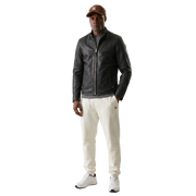 Men's black leather jacket with zipper, paired with cream joggers and white sneakers, styled with a brown cap.