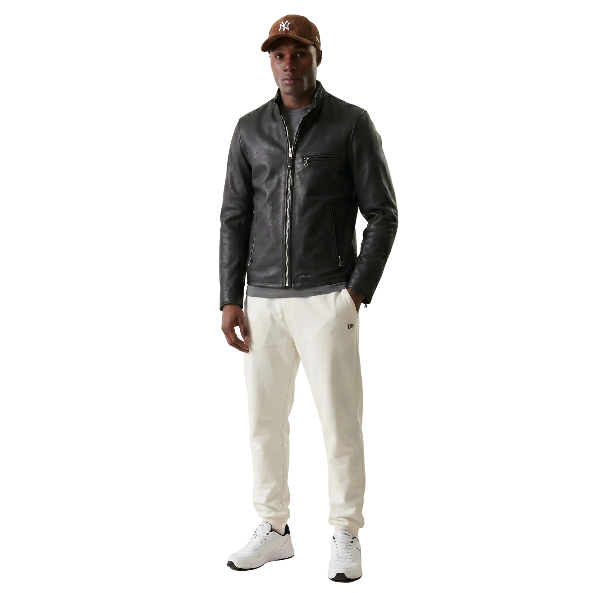 Men's black leather jacket with zipper, paired with cream joggers and white sneakers, styled with a brown cap.