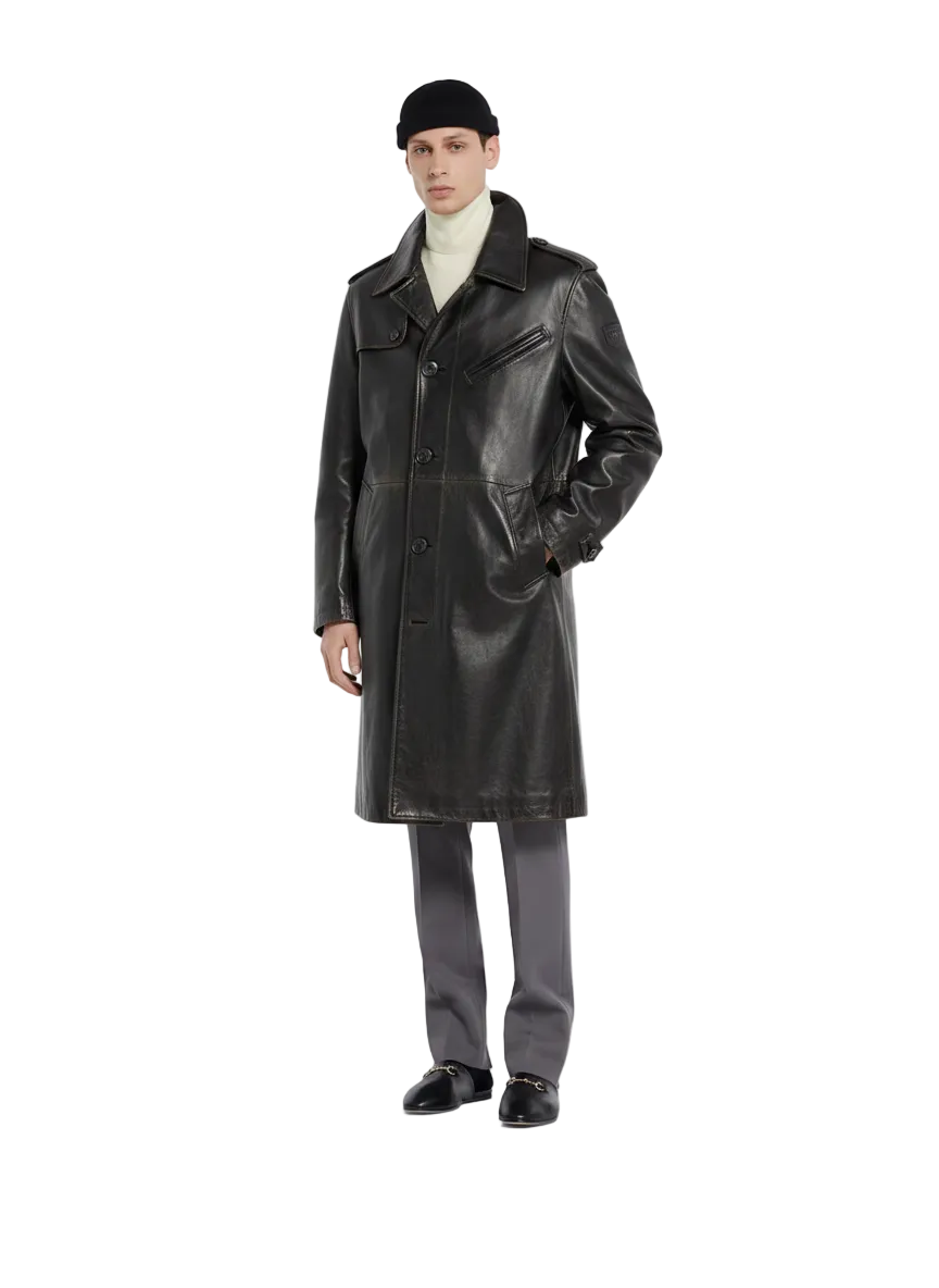 Men's black leather trench coat with classic collar and front buttons, styled with turtleneck and gray trousers