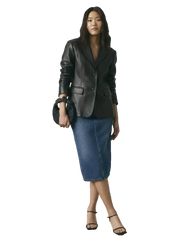 Woman wearing black leather blazer, denim midi skirt, and black heels with a matching handbag.