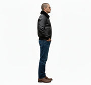 Man in black leather bomber jacket with shearling collar, blue jeans, and brown boots, side profile