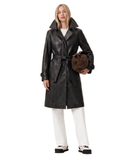 Black leather trench coat with belt, paired with white pants and sneakers, holding a brown bag