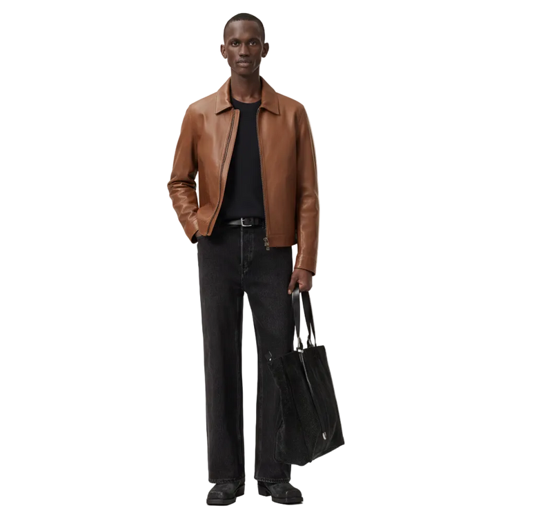 Man wearing a brown leather jacket and black pants holding a black bag on a white background